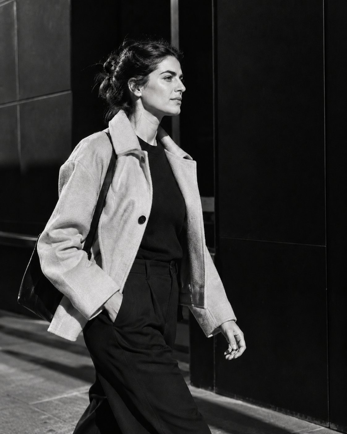 Zwart-witfoto van een vrouw onderweg langs een donkere gevel in de stad