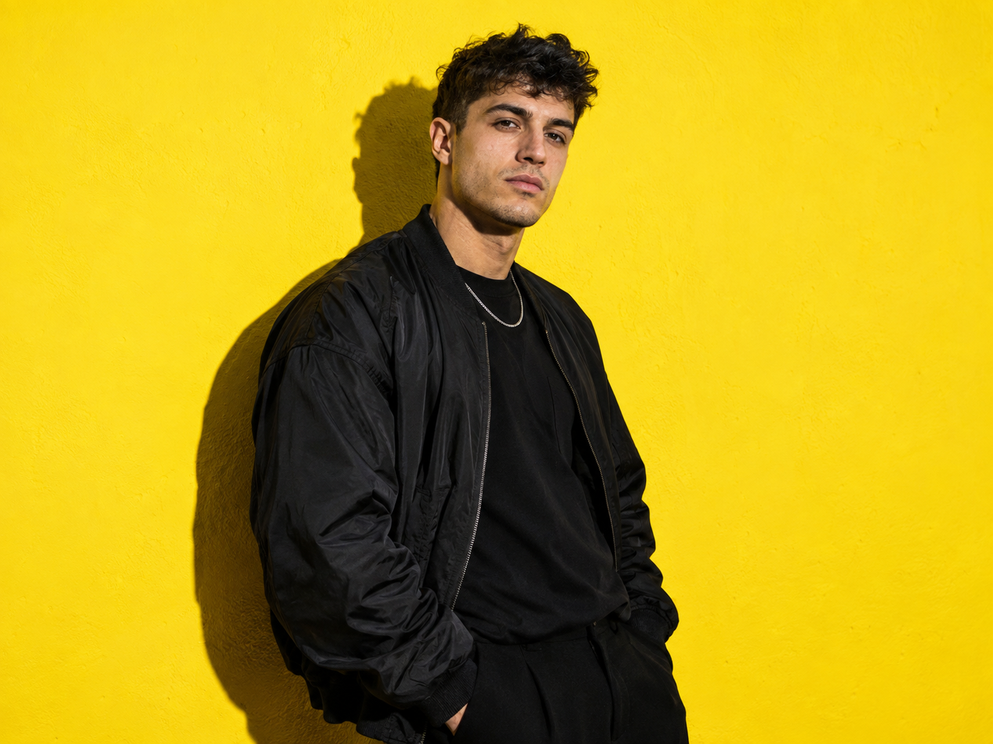 Jongen in zwarte streetwear tegen een gele achtergrond